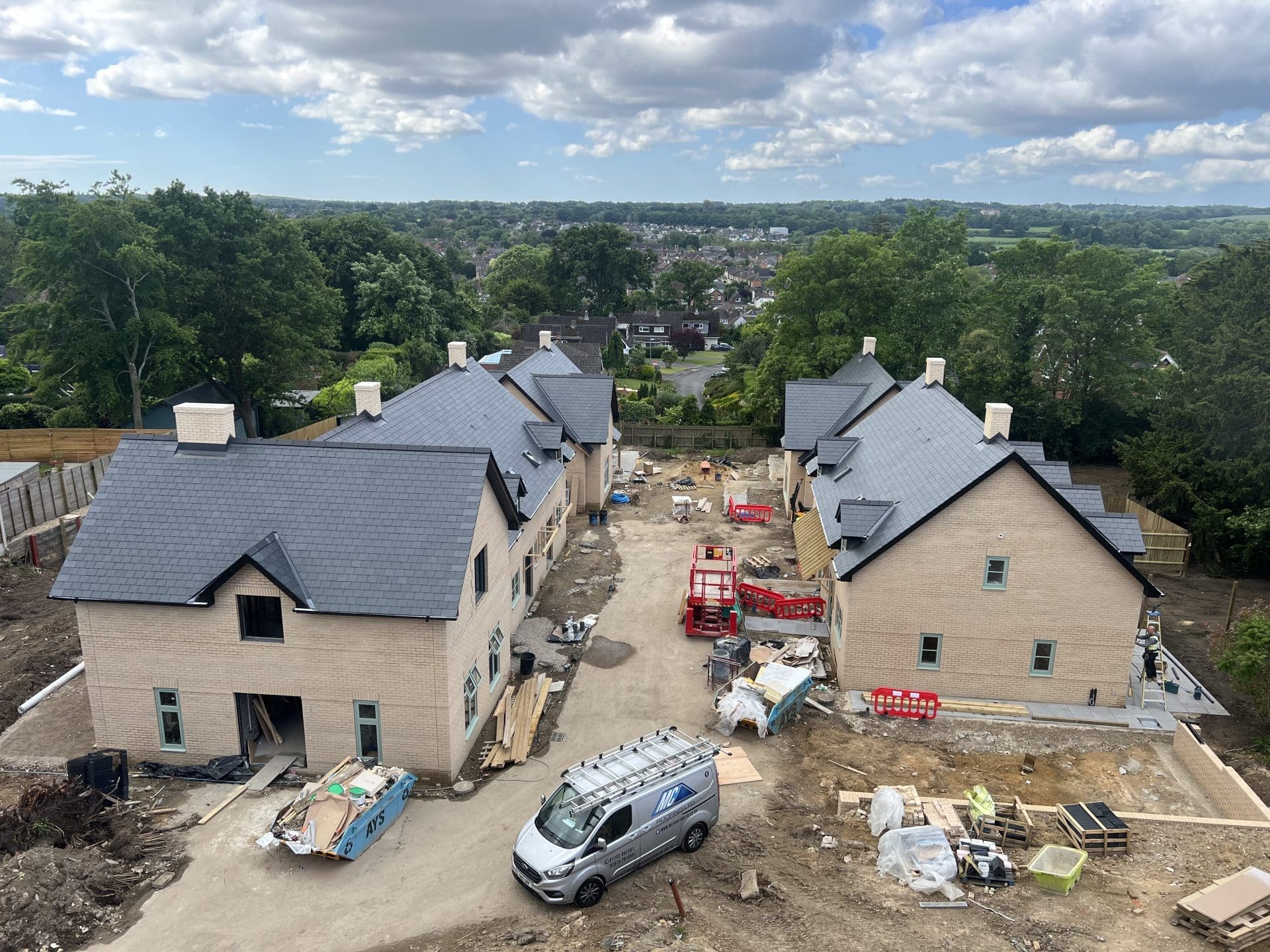 New housing development with premium slate roofing installation Drone view of multiple newly built residential properties featuring expertly installed slate roofing, surrounded by construction equipment and landscaped plots in progress